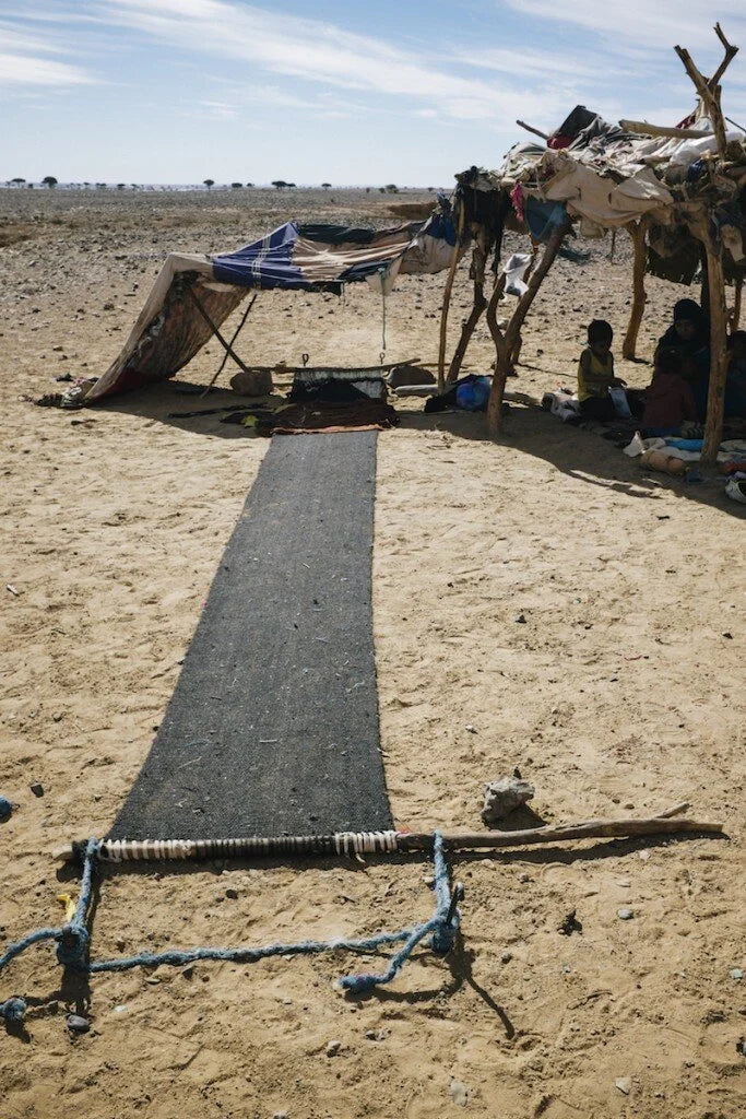 The fabric is laid out on the ground, each panel a step closer to becoming a fully-formed Bedouin tent, ready to shelter from the desert's elements.